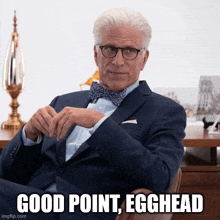 a man in a suit and bow tie is sitting at a desk with the words good point egghead below him