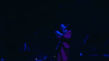 a man in a red shirt is singing into a microphone with blue lights behind him