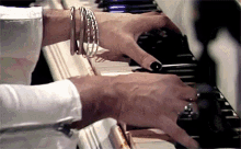 a woman with black nails is playing a piano while wearing bracelets