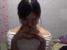 a woman making a heart with her hands in front of a hello kitty wallpaper