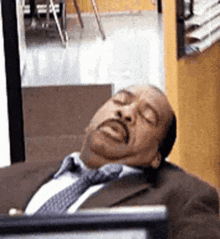 a man in a suit and tie is sleeping in front of a computer .