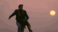 a man in a blue jacket and scarf is walking in front of a sunset