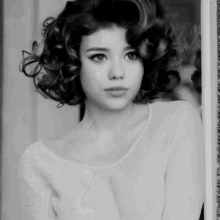 a woman with curly hair is wearing a white top