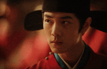 a man wearing a black hat and a red shirt looks at the camera