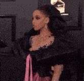 a woman in a black and pink dress is standing on a red carpet at a grammy awards event .