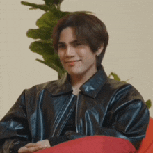 a young man wearing a black leather jacket is sitting on a red cushion .