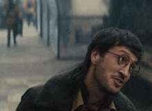 a man wearing glasses and a mullet looks to his left