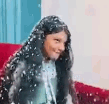 a young girl with long black hair is sitting on a red couch covered in foam .
