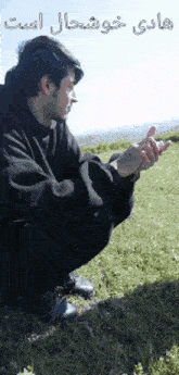 a man in a black hoodie is squatting down in a field