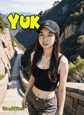 a girl wearing a baseball cap and a crop top stands in front of a mountain with the word yuk written above her