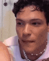 a man with curly hair is wearing a pearl necklace and making a funny face .