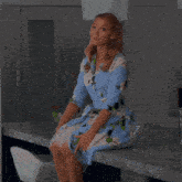 a woman wearing a blue floral dress sits on a counter