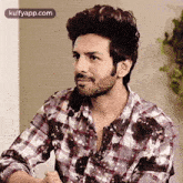 a man with a beard is wearing a plaid shirt and sitting in a chair .