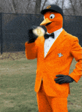 a mascot wearing an orange suit and black hat holds a gold coin