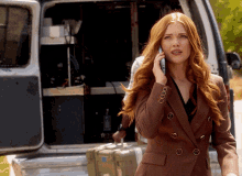 a woman with red hair is talking on a cell phone in front of a van