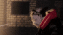 a man in a red jacket is standing in a dark room with a brick wall in the background .