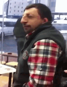 a man wearing a plaid shirt and a vest with a badge on it