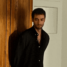 a man in a black shirt is leaning against a wooden door