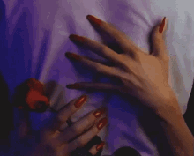 a woman with long red nails is holding a red rose in her hand .