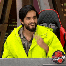 a man in a neon yellow jacket is sitting at a desk with a sticker that says charged