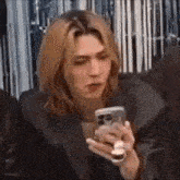 a young man with long hair is holding a cell phone in his hand .
