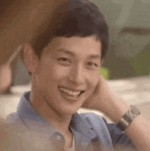 a young man is smiling and touching his face with his hand while wearing a watch .