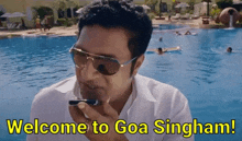 a man talking on a cell phone in front of a pool with the words welcome to goa singham written below him