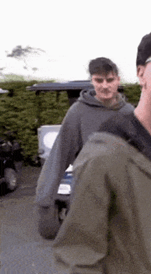 a man in a grey hoodie is standing next to another man in a green jacket .