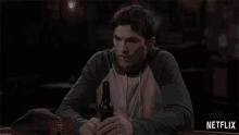 a man sitting at a table with a bottle of beer and a netflix logo in the corner
