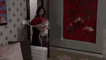 a woman in a robe is holding a bouquet of red roses in a bedroom .