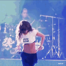 a woman in a crop top is dancing on a stage with a band behind her
