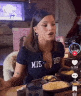 a woman wearing a shirt that says mis bhy is sitting at a table
