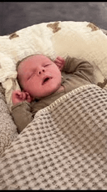a baby is sleeping in a crib under a blanket with his mouth open .