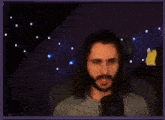 a man with long hair and a beard is sitting in front of a microphone and making a face .