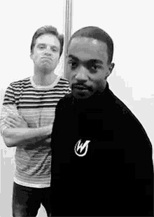 two men are standing next to each other with their arms crossed . one of the men is wearing a striped shirt .