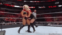 two women are wrestling in a wrestling ring while a referee looks on .