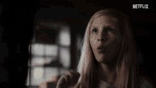 a girl with blonde hair is looking up in a dark room with a netflix logo behind her