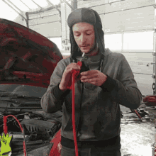 a man wearing a hat is holding a red hose in front of a car with the hood open
