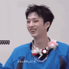 a young man wearing a blue shirt and a necklace with stuffed animals on it is smiling .