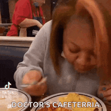a woman sitting at a table with a plate of food that says doctor 's cafeteria on it