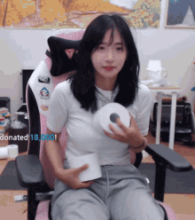 a woman is sitting in a pink chair holding a roll of toilet paper with the words donated 18,000 below her