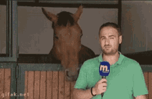 a man holding a microphone in front of a horse in a stable .