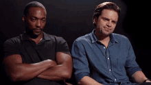 two men are sitting next to each other with their arms crossed and looking at each other .