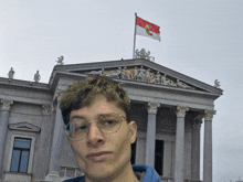a man stands in front of a large building with a flag on top of it