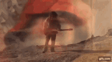 a man is playing a guitar in front of a fire while standing in the dirt .