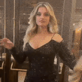 a woman in a black dress is standing in front of a door waving .