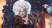a drag queen with a large white wig is pointing her finger