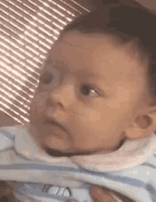 a baby in a striped shirt is being held by a person and looking at the camera .