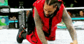 a wrestler is kneeling on the ground in a ring .
