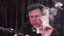 elon musk is smoking a joint in front of a microphone while wearing headphones .